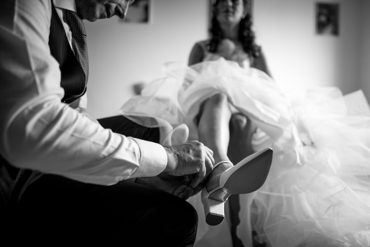 il padre della sposa che infila le scarpe alla sposa prima del matrimonio