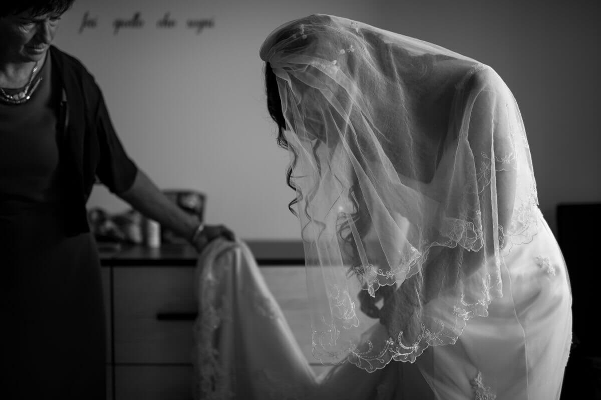 la sposa con il velo mentre si sistema il vestito con lo strascico