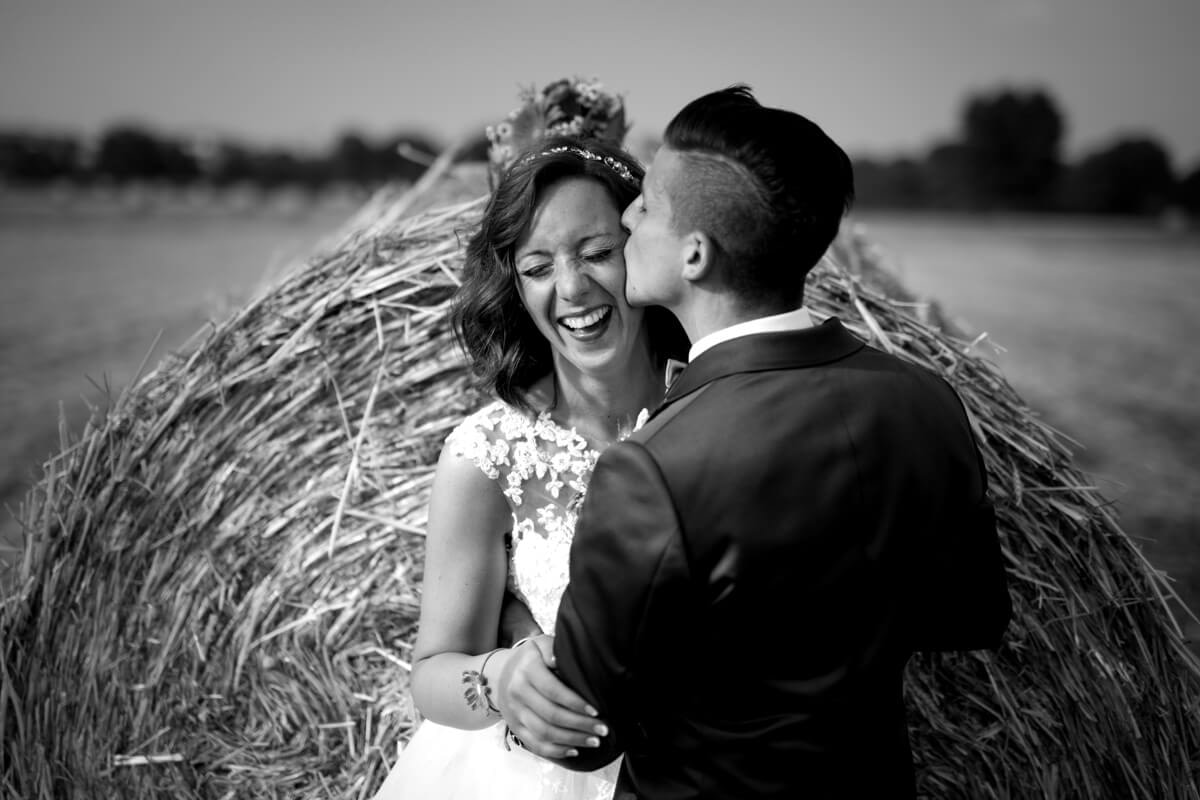 lo sposo bacia sulla guancia la sposa mentre ride in un campo di grano