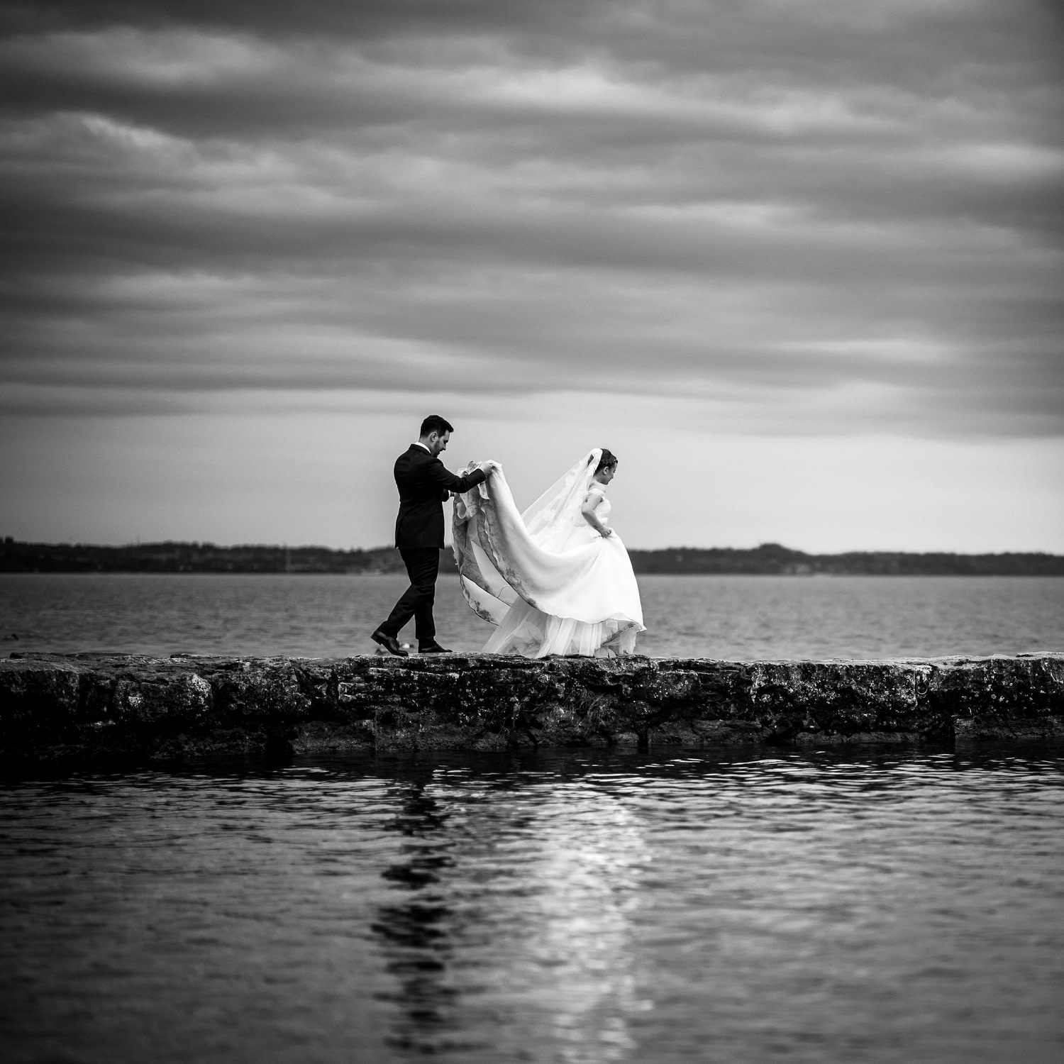 lo sposo tiene il vestito alla sposa mentre camminavano sulla passerella sopra al lago