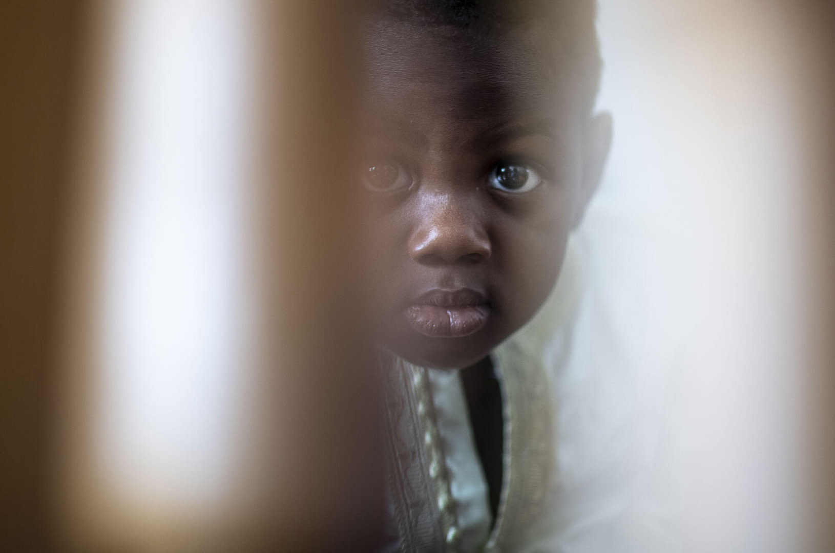 un bambino di origine africana guarda il fotografo da dietro una porta
