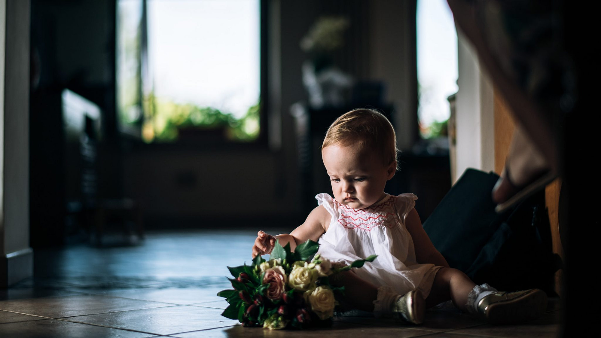una bambina piccola seduta sul pavimento gioca con il bouquet della sposa