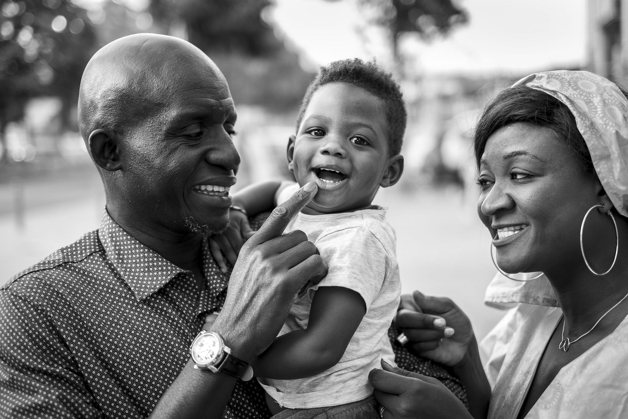 un bambino di origine africana sorride divertito mentre è in braccio al papà con la mamma accanto