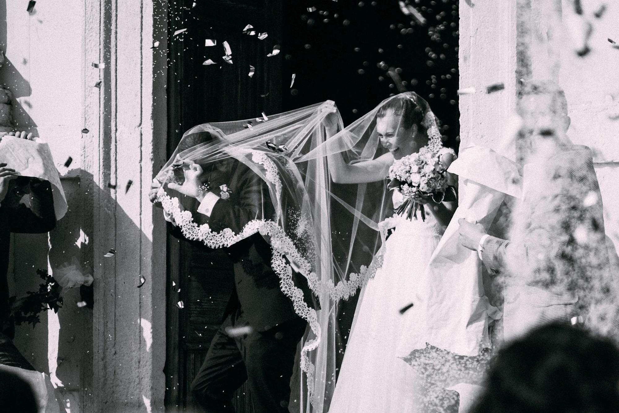 gli sposi all'uscita dalla chiesa durante il lancio del riso si coprono con il velo del vestito